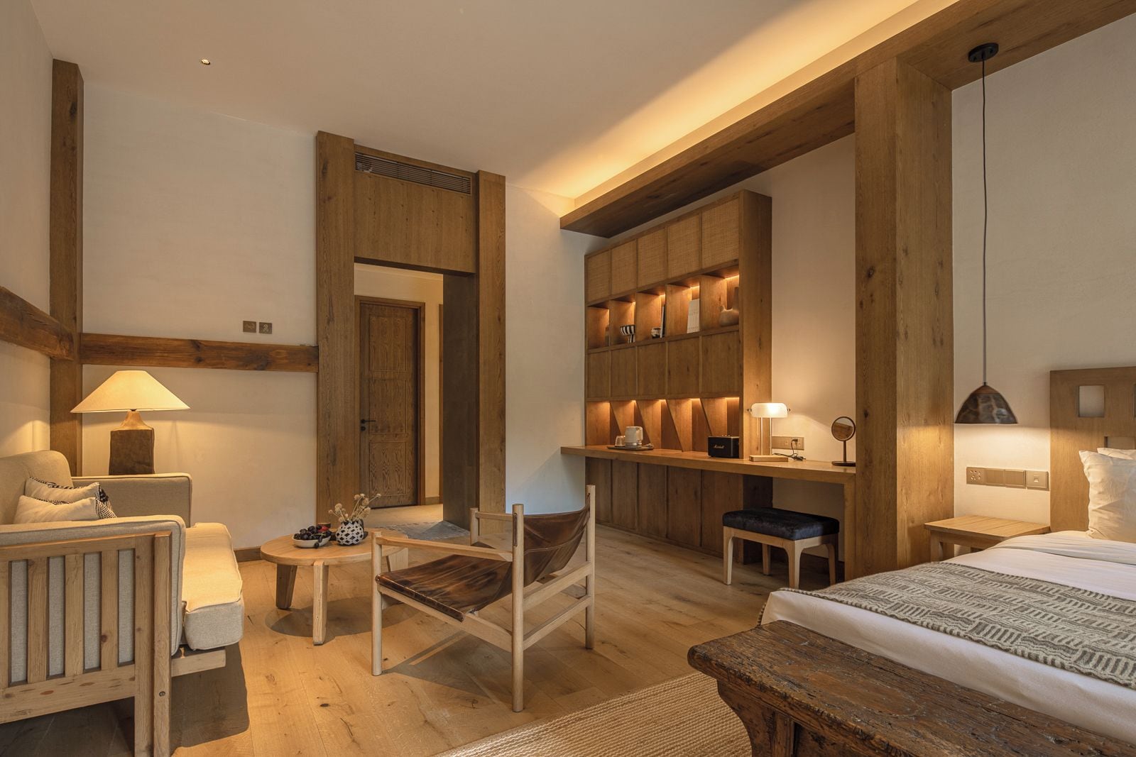 A hotel room with a wooden bed, a desk, a chair, a sofa, and a kitchenette area.