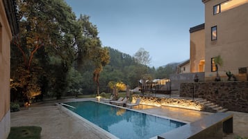 A swimming pool with lounge chairs, surrounded by trees and a stone wall.