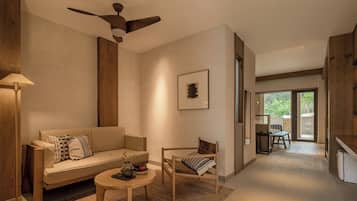 A modern living room with a sofa, a coffee table, and a chair. There is a ceiling fan, a framed picture on the wall, and a view of the outdoors through a glass door.