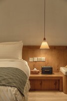 A bedroom with a bed, a nightstand with a lamp, a Marshall speaker, and a wooden headboard.