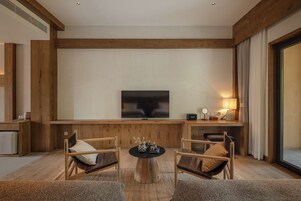 A modern living room with a flat-screen TV, wooden furniture, a coffee table, and a lamp.