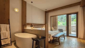 A modern bathroom with a large bathtub, a wooden bench, and a table with a view of the outdoors.