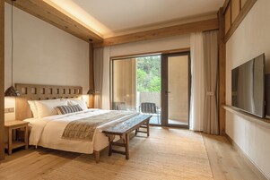 A bedroom with a bed, bedside table, bench, and a TV mounted on the wall.