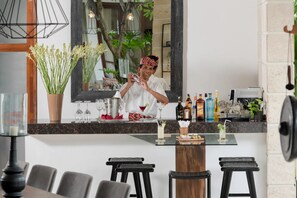 A bar area with a bartender preparing drinks, a variety of bottles, glasses, and a potted plant. - Casa Brio (Badung)