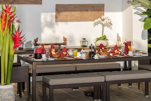 A breakfast setup with a wicker table, benches, and a variety of breakfast items. - Casa Brio (Badung)
