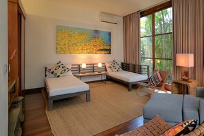A hotel room with two beds, a sofa, a window with curtains, and a painting on the wall. - Casa Brio (Badung)