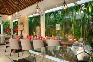 A dining area with a glass table, chairs, and a tropical plant backdrop. - Casa Brio (Badung)