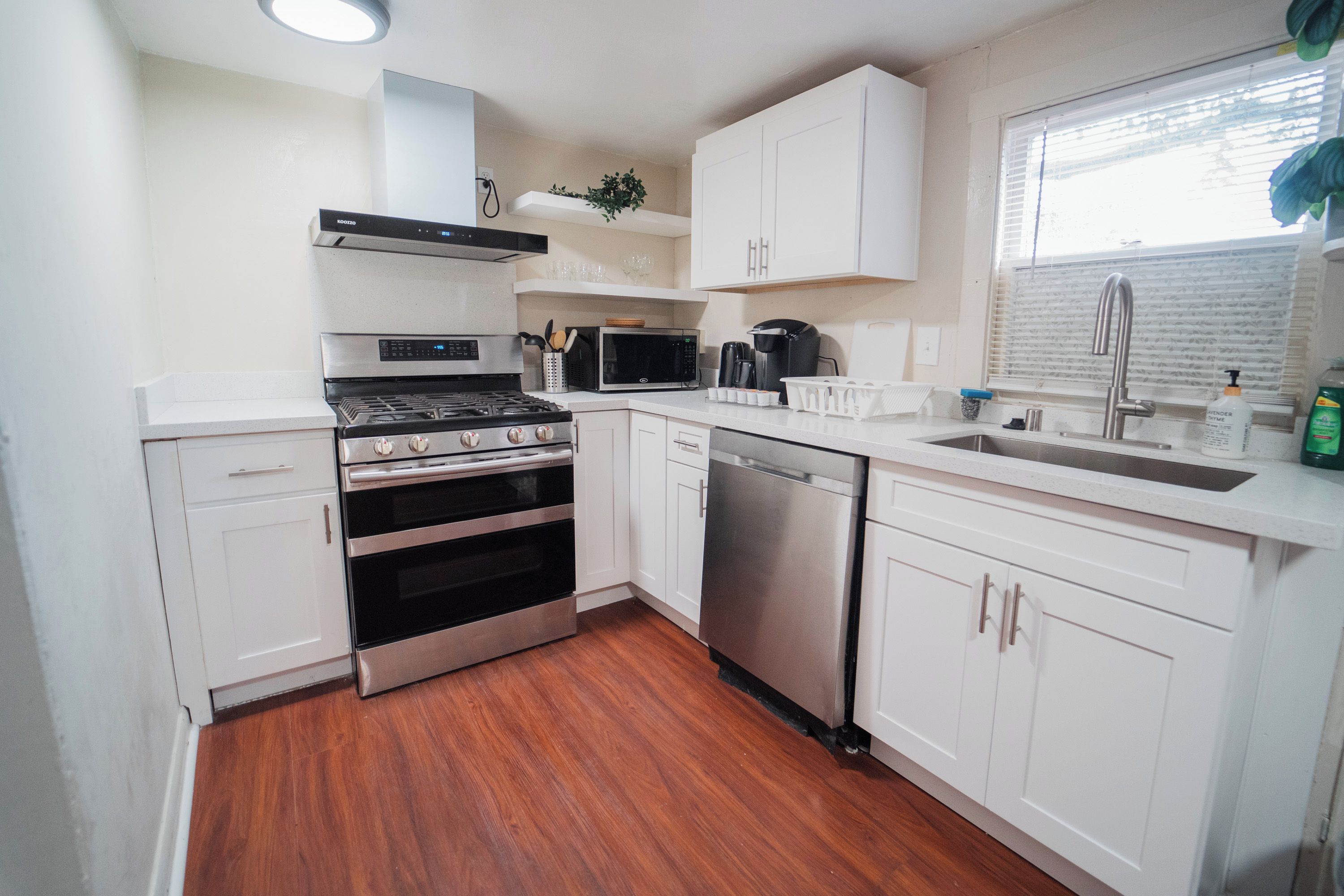 A compact kitchen with white cabinets, a stainless steel stove, a microwave, and a dishwasher.