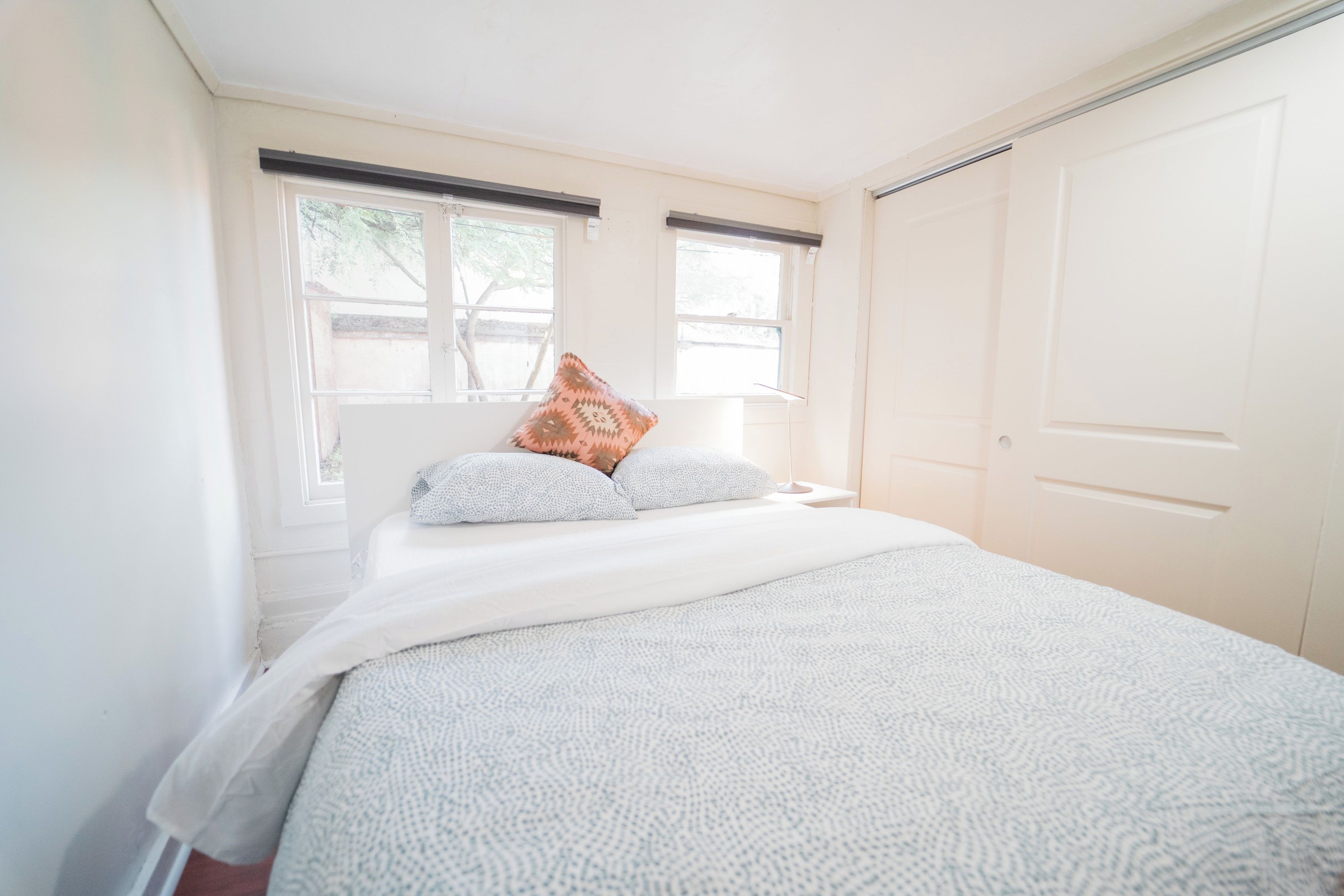 A bedroom with a bed, two windows, a door, and a nightstand.