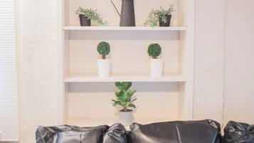 A black leather sofa with three cushions, a white shelving unit with potted plants, and a white wall.