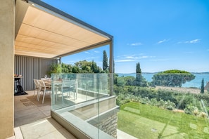 A modern outdoor dining area with a glass balustrade overlooking a lake and lush greenery. - Demeures Kokio 100 m. From Sandy Beach (Grimaud)