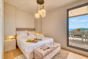 A bedroom with a bed, bedside tables, a reading bench, and a large window with a view. - Demeures Kokio 100 m. From Sandy Beach (Grimaud)