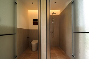 Et stilfuldt badeværelse med en brusekabine i glas, toilet og en lille hylde.