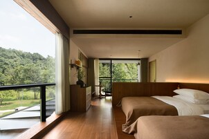 A modern bedroom with two beds, a balcony, and a view of a forested area.