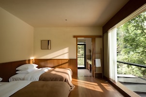 A hotel room with a large window, a bed, a bedside table, and a view of greenery outside.