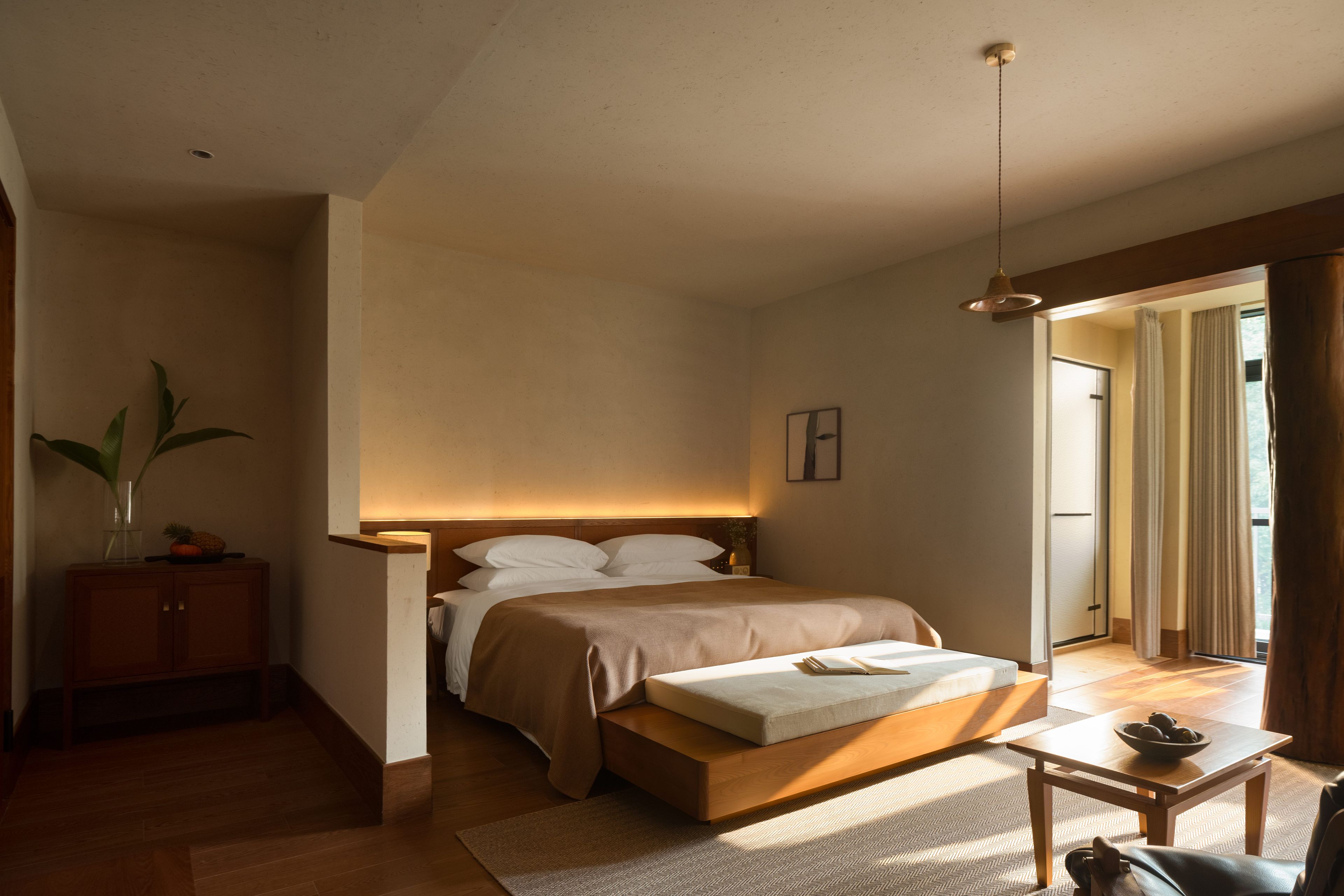 A bedroom with a bed, bedside table, and a view of the outside.