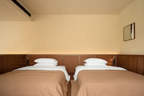 Habitació d'hotel amb dos llits individuals, ambres de fusta, un mirall fixat a la paret i un registre al sostre.