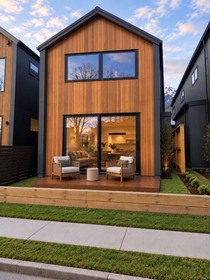 Ein modernes, zweistöckiges Haus mit Holzfassade, großen Fenstern und einer Terrasse mit Gartenmöbeln.