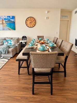 A dining area with a wooden table set for four, a clock on the wall, and a sofa with cushions. - Spacius 3 bedroom-Ocean View Luxe Stay•Downtown Fort Myers•Pool •Spa (Fort Myers)