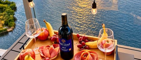 A balcony with a sunset view, a bottle of wine, and a tray of fruits and cheese.