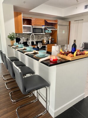 A modern kitchen with a central island, bar stools, and a dining area. - Spacius 3 bedroom-Ocean View Luxe Stay•Downtown Fort Myers•Pool •Spa (Fort Myers)