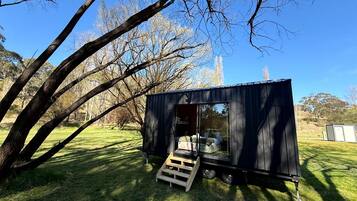 A small, black, metal structure with a sliding door, a wooden ramp, and a clear view of the interior.