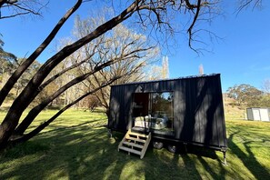 A small, black, metal structure with a sliding door, a wooden ramp, and a clear view of the interior.