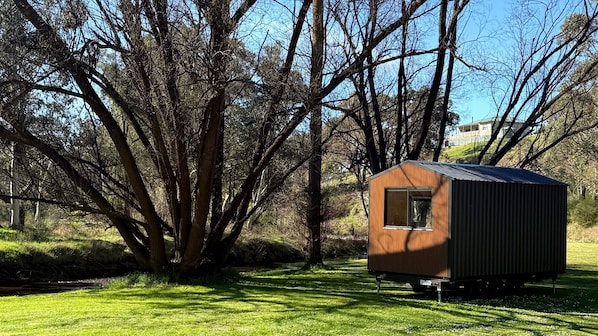 A small, single-story structure with a sloped roof, situated in a grassy area with trees in the background.