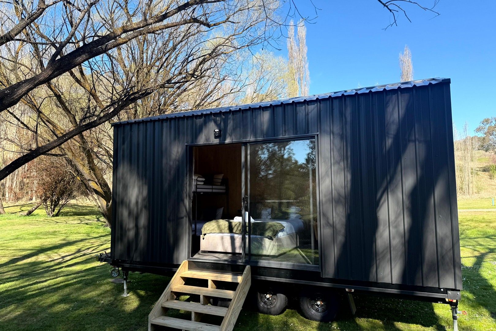 Una casa móvil pequeña y oscura de color oscuro, con una puerta corredera, una cama en el interior y una rampa de madera que la lleva hasta arriba.