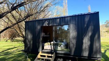 Una casa móvil pequeña y oscura de color oscuro, con una puerta corredera, una cama en el interior y una rampa de madera que la lleva hasta arriba.