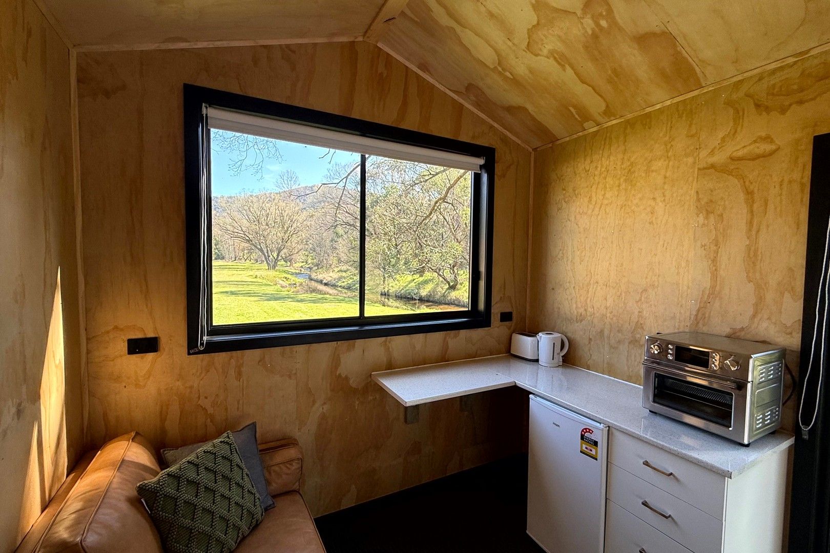 Una cocina compacta con horno integrado, un refrigerador pequeño y un ventanal con vistas a un paisaje verde.