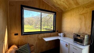 Una cocina compacta con horno integrado, un refrigerador pequeño y un ventanal con vistas a un paisaje verde.