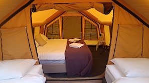 A tented accommodation with a bed, pillows, and a chair.