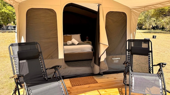 A tent with a bed and two chairs inside.