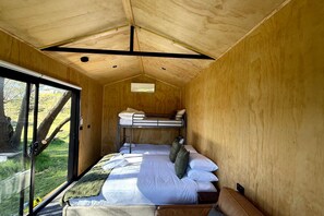 A compact wooden cabin with a bunk bed, a glass door leading outside, and a small window.