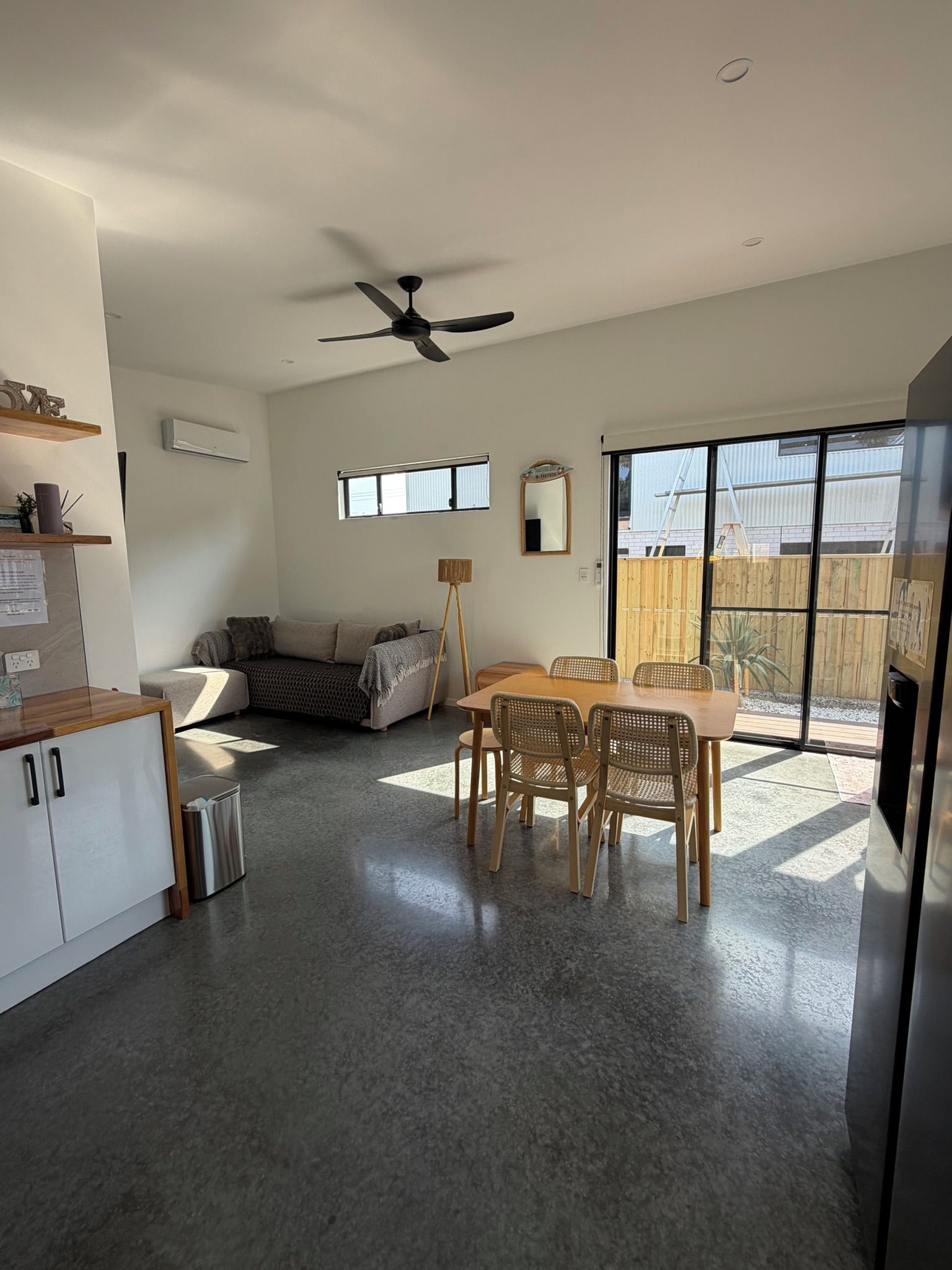 A spacious living area with a dining table and chairs, a sofa, a ceiling fan, and a sliding glass door leading to a backyard.