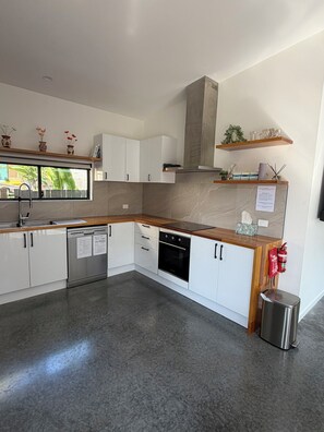 Una cocina moderna con armarios blancos, un lavavajillas de acero inoxidable, horno empotrado y encimera de madera.