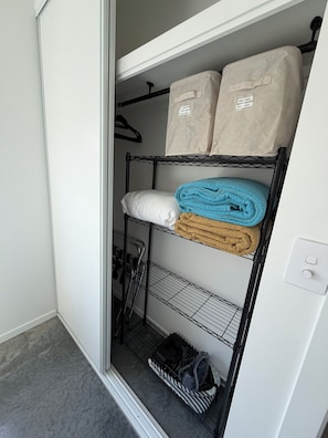 Un armario con estantes que contienen ropa de cama doblada, un zapatero y una barra para colgar bolsos.