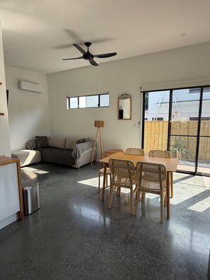 A spacious living area with a dining table, chairs, a sofa, a standing lamp, and a ceiling fan.