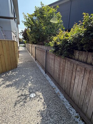 A gravel driveway leading to a wooden fence with dense foliage.