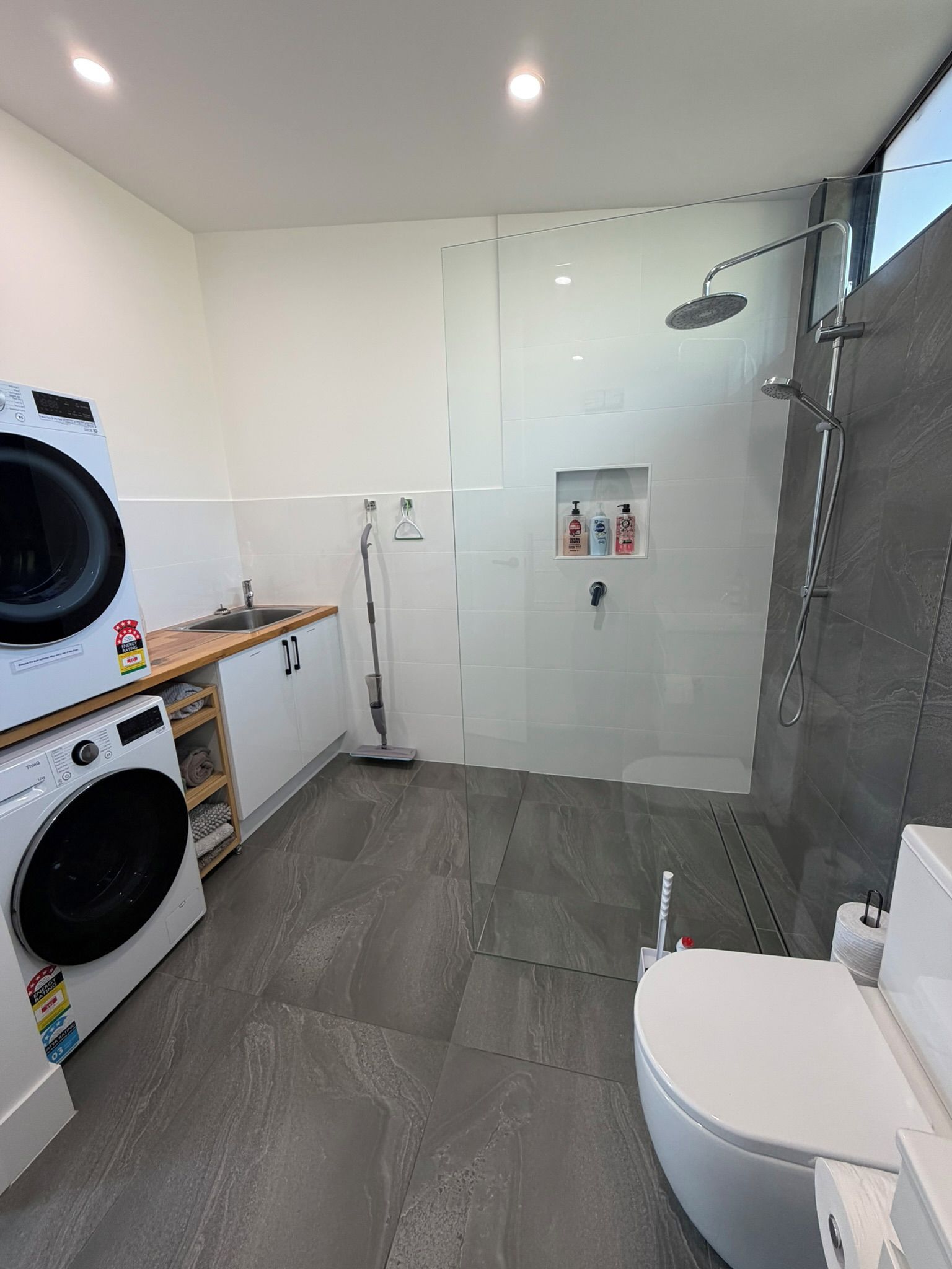 A modern bathroom with a glass-enclosed shower, a washing machine, a toilet, and a sink.