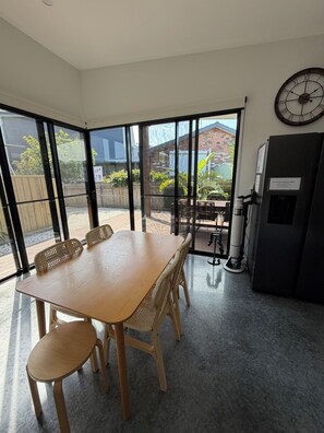 A modern kitchen with a large dining table, chairs, a refrigerator, and a clock on the wall.