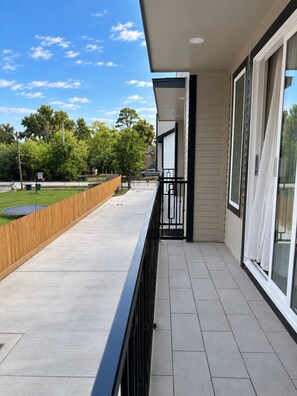 A balcony with a view of a grassy area and trees, a wooden fence, and a clear sky. - NEW 2BR Luxury Townhome Gated + Garage 10 Min DT (Houston)