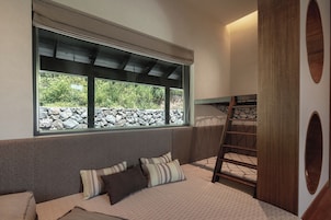 Una habitación con literas, una ventana con vistas a zonas verdes y una escalera de madera.