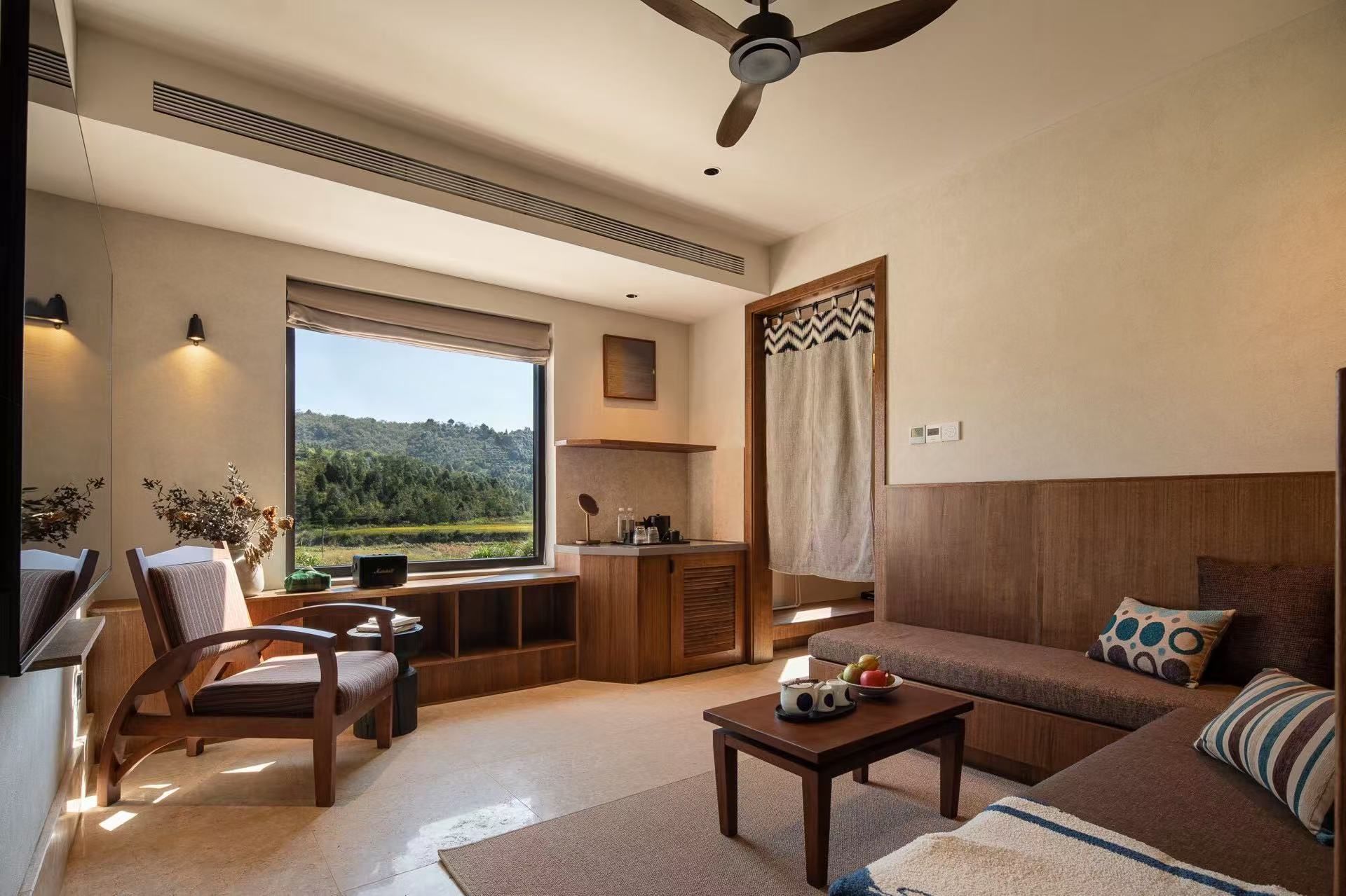 Una sala de estar moderna con un sofá, una mesa de centro y una silla. Hay un ventanal con vistas a zonas verdes.