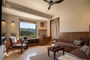 Una sala de estar moderna con un sofá, una mesa de centro y una silla. Hay un ventanal con vistas a zonas verdes.