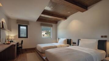 A bedroom with two beds, a desk, and a window.