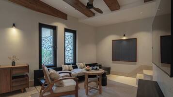 A modern living room with a sofa, chairs, a coffee table, and a fireplace. There are two windows with stone frames and a ceiling fan.