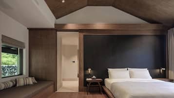 Un dormitorio moderno con una cama grande, un rincón de descanso con cojines y vistas al verdor por una ventana.