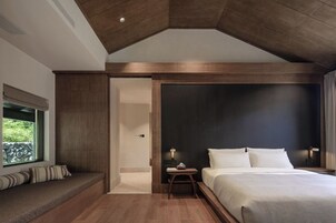 Un dormitorio moderno con una cama grande, un rincón de descanso con cojines y vistas al verdor por una ventana.